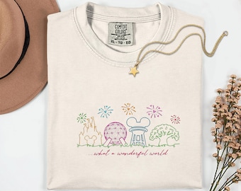 May include: Cream-colored Comfort Colors t-shirt with a colorful line drawing of a castle, Spaceship Earth, and other landmarks. The text "...what a wonderful world" is below the drawing. A gold star pendant necklace is on the shirt.