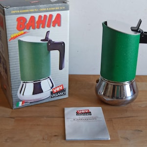 May include: A green and silver stovetop espresso maker with a black handle and a white lid. The coffee maker is next to its original box, which has the word "BAHIA" in red and the brand name "VEV VIGANO". A small booklet is also present.