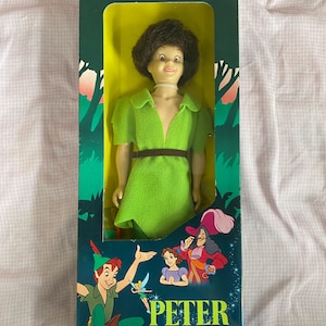 May include: A vintage Walt Disney's Peter Pan doll in its original box. The doll is wearing a green shirt and brown pants. The box features a green background with illustrations of Peter Pan, Captain Hook, and Tinkerbell. The text "PETER PAN" is printed in large, bold letters on the box.