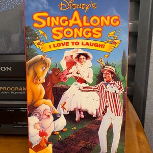 May include: A Disney's Sing Along Songs VHS tape titled "I Love to Laugh!" featuring cartoon characters and musical notes. The cover has a blue background with the words "Volume Nine" at the bottom.
