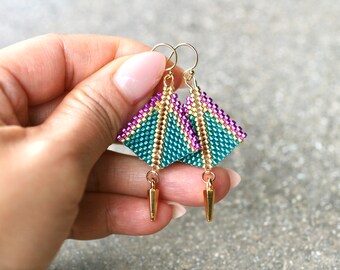 May include: A pair of geometric dangle earrings with a teal, gold, and purple color scheme. The earrings are made with small beads and have a gold teardrop-shaped pendant.