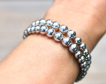 May include: A silver beaded bracelet with two rows of round beads. The bracelet is worn on a person's wrist.