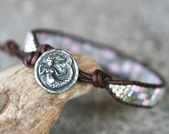 May include: A brown leather bracelet with a silver mermaid charm and pink, green, and silver beads.