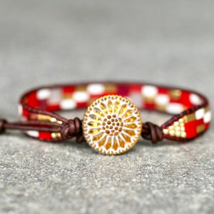May include: Red, white, and gold beaded bracelet with a decorative button closure. The button has a gold-toned, circular design with a white center.