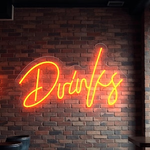 Peut inclure: Une enseigne au néon jaune vif épelle "Drinks" sur un mur de briques. L'enseigne est le point central, avec un bar et des tabourets au premier plan et une fenêtre à droite.
