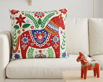 May include: A square throw pillow featuring a red horse illustration with blue, green, and white floral patterns, accompanied by a small red horse figurine. The pillow displays a central heart motif and intricate botanical designs on a cream background.