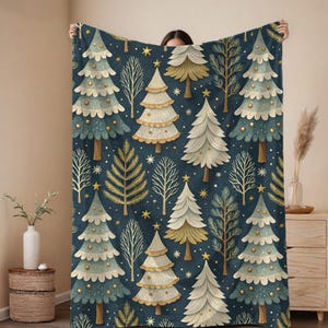 May include: A rectangular throw blanket featuring a dark blue background with a repeating pattern of stylized Christmas trees in shades of cream, gold, and muted green, interspersed with bare winter trees and small gold stars throughout.
