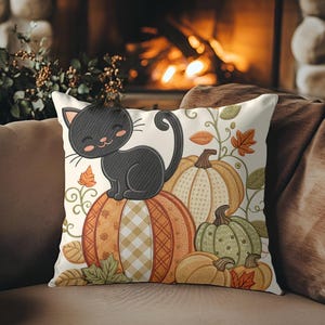May include: A decorative throw pillow featuring a black cat sitting atop a collection of pumpkins. The pumpkins are in shades of orange and green, with fall leaves and vines. The pillow has a cream background and is placed on a brown sofa.