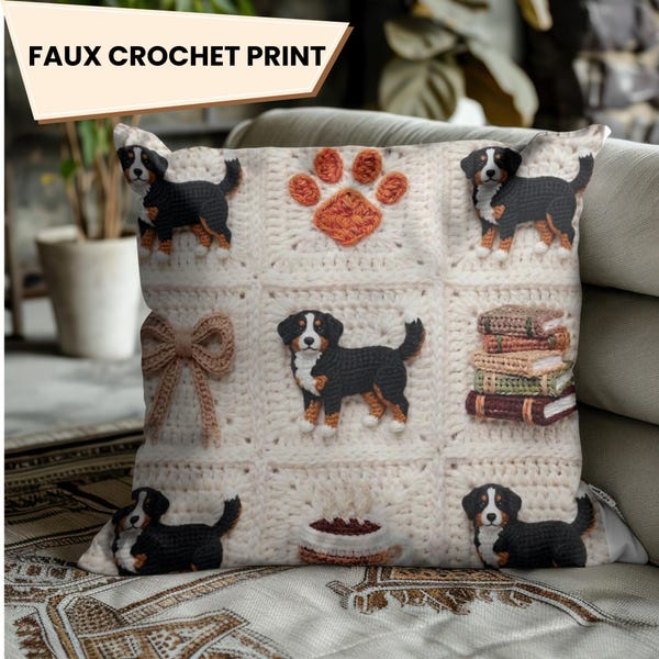 Könnte beinhalten: Ein quadratisches Zierkissen mit einem Faux-Häkel-Druck auf cremefarbenem Hintergrund. Das Design besteht aus wiederkehrenden Rasterquadraten mit Abbildungen von Berner Sennenhunden, einer Pfote, einer Schleife, einem Bücherstapel und einer Kaffeetasse.