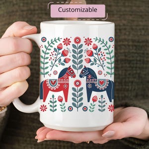 May include: White ceramic mug with a red and blue Scandinavian folk art design featuring two stylized horses and floral patterns.