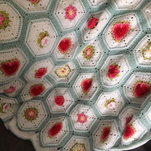 May include: A crocheted blanket with a hexagonal pattern featuring a variety of flowers in shades of pink, red, green, and yellow.