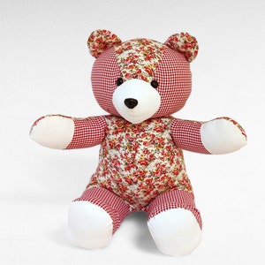 Op de afbeelding: Een patchwork teddybeer met rood-wit geruit stof en een bloemenprint. De beer heeft witte poten en een wit gezicht.
