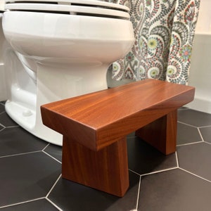 May include: A solid wood bathroom step stool with a rich reddish-brown finish. The stool has a rectangular top and two angled legs.