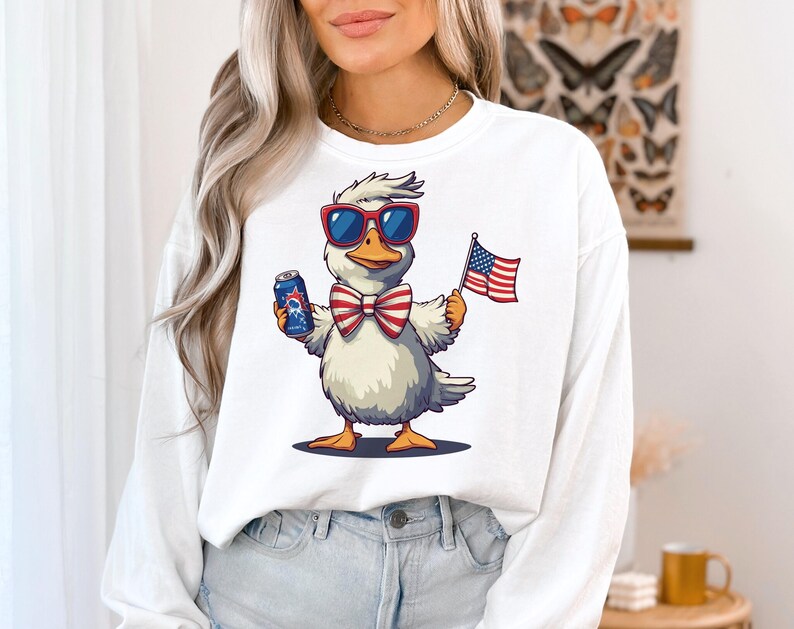 May include: White long-sleeved shirt with a cartoon duck wearing sunglasses, a bow tie, and holding a can and an American flag.
