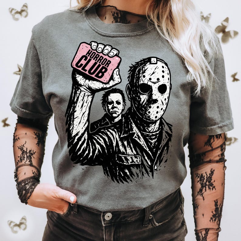 Pu&ograve; includere: T-shirt grigia con grafica di Jason Voorhees di Venerd&igrave; 13, che tiene in mano un cartello rosa con la scritta "HORROR CLUB". Il design include anche Michael Myers. Girocollo.