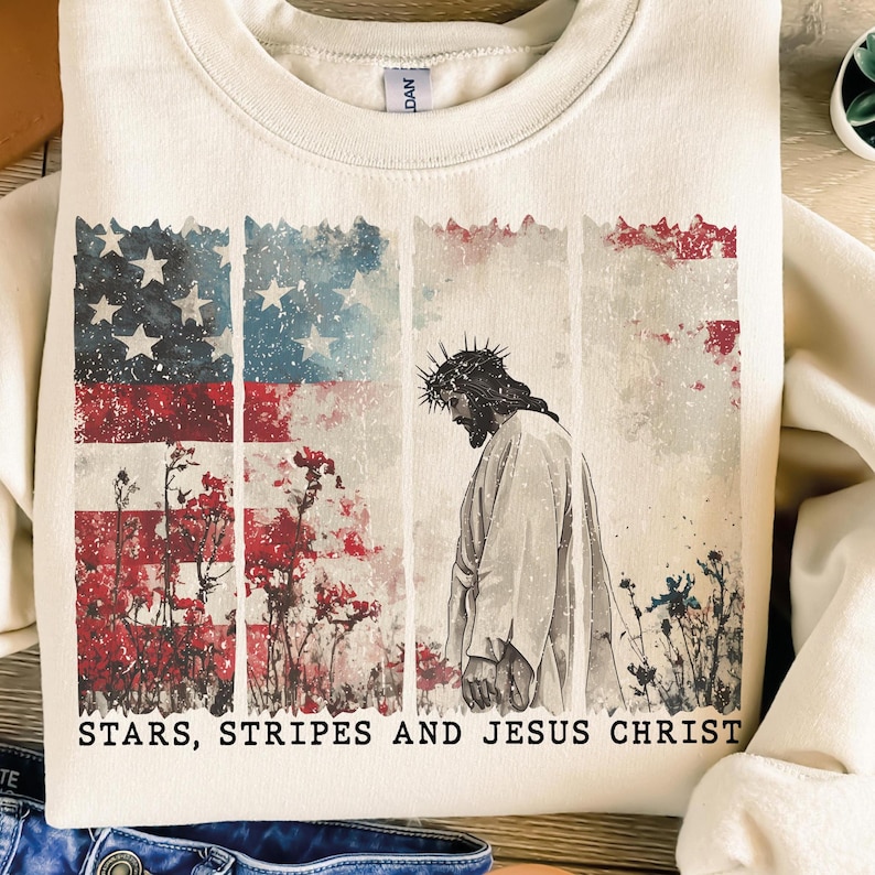 May include: Cream-colored sweatshirt featuring a distressed American flag design with red, white, and blue colors. The graphic includes an illustration of Jesus Christ and the text "STARS, STRIPES AND JESUS CHRIST".