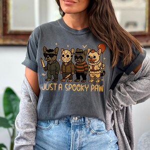 May include: Dark gray t-shirt featuring a graphic of four cartoon French Bulldogs dressed in Halloween costumes. The phrase "JUST A SPOOKY PAW" is printed below the dogs. The dogs are dressed as a killer, Jason, Freddy Krueger, and a clown.