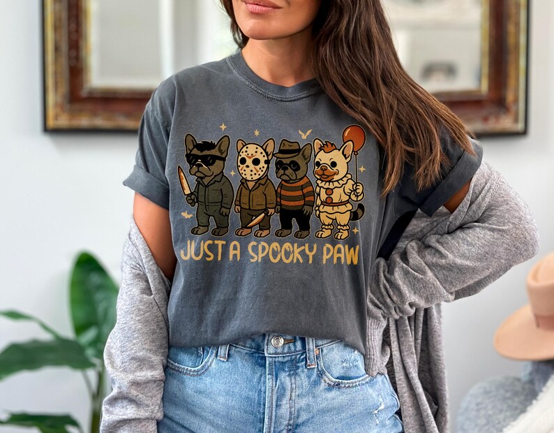 May include: Dark gray t-shirt featuring a graphic of four cartoon French Bulldogs dressed in Halloween costumes. The phrase "JUST A SPOOKY PAW" is printed below the dogs. The dogs are dressed as a killer, Jason, Freddy Krueger, and a clown.