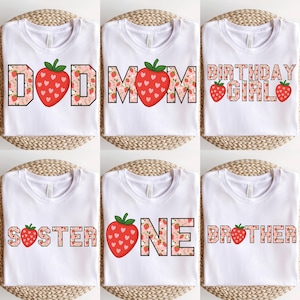 May include: Six white t-shirts with different strawberry-themed designs. The designs include "DAD", "MOM", "BIRTHDAY GIRL", "SISTER", "ONE", and "BROTHER".