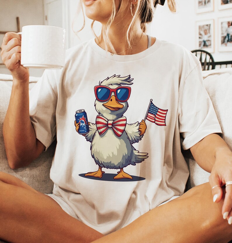 May include: White t-shirt with a cartoon duck wearing sunglasses and a red, white, and blue bow tie. The duck is holding a can of beer and a small American flag.