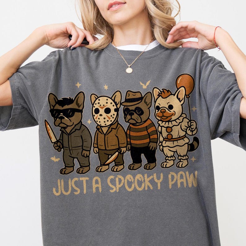 May include: Gray t-shirt with a graphic of four cartoon French Bulldogs dressed as horror movie characters. The phrase "JUST A SPOOKY PAW" is printed below the dogs. The dogs are wearing sunglasses, a hockey mask, a hat, and a clown costume.