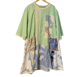 May include: A light green patchwork dress with short sleeves, lace trim, and multiple pockets. The dress features a variety of floral and patterned fabrics in shades of blue, white, and red. The dress is hanging on a wooden hanger.
