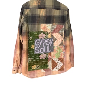 May include: A plaid flannel shirt with patchwork details. The back features a green floral patch with the text "Gypsy Soul" and a patchwork design. The shirt has a faded, distressed look with a mix of colors.