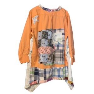 May include: Orange long-sleeved shirt with patchwork design. The patchwork includes various patterns and colors, including floral, plaid, and polka dots. A white bird applique is on the upper left chest. The shirt has a unique, asymmetrical hemline.