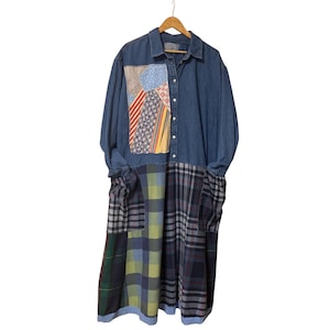 May include: A long denim dress with a patchwork design on the bodice and a plaid pattern on the lower half. The dress has long sleeves and a button-down front. The patchwork includes various patterned fabrics in red, blue, yellow, and white.