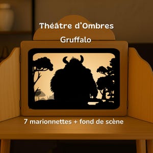 Peut inclure: Un théâtre d'ombres en bois avec le texte Théâtre d'Ombres Gruffalo et 7 marionnettes + fond de scène. L'écran rétroéclairé montre la silhouette noire d'une créature à cornes dans une forêt avec des arbres et des champignons.