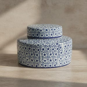 May include: A blue and white ceramic jar and lid set. The jar is cylindrical with a rounded base, and the lid is a smaller, matching cylinder. Both pieces are decorated with a repeating floral pattern. The design is a repeating pattern of small, stylized flowers.