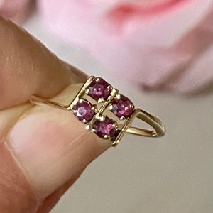 May include: A gold ring with a square-shaped setting featuring six small, deep pink gemstones.