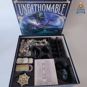 Può includere: Scatola di gioco da tavolo aperta intitolata "Unfathomable" con un coperchio blu scuro con un'illustrazione di un mostro marino. All'interno, vari componenti del gioco sono organizzati in vassoi neri, tra cui carte, gettoni e miniature. È visibile un gettone a forma di timone.