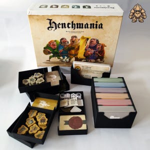 Könnte beinhalten: Ein schwarzer Organizer mit mehreren Fächern zum Verstauen von Spielfiguren und Karten. Der Organizer ist für das Brettspiel "Henchmania" konzipiert.