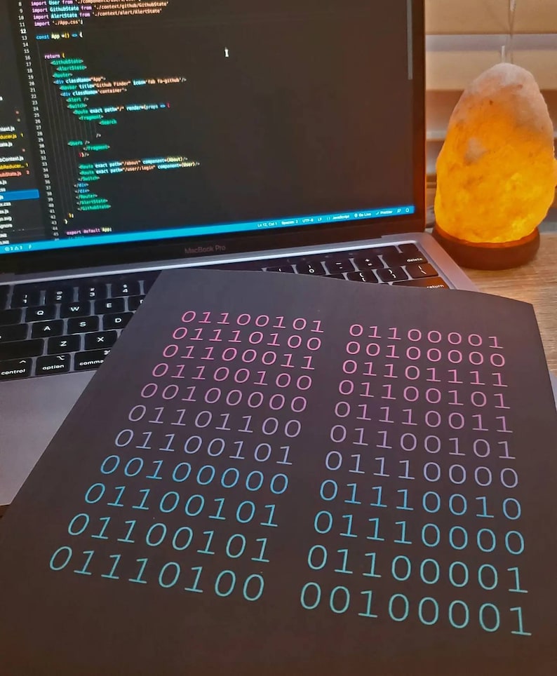 K&ouml;nnte beinhalten: Ein schwarzes Notizbuch mit einem bin&auml;ren Code, der in Rosa und Blau auf dem Cover gedruckt ist. Der Code ist in Spalten und Zeilen angeordnet.