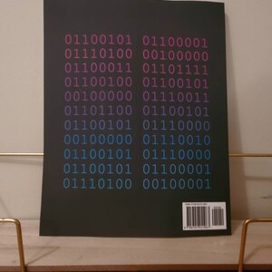 K&ouml;nnte beinhalten: Ein schwarzer Buchumschlag mit einem Muster aus bin&auml;rem Code in Pink, Blau und Wei&szlig;. Der Code ist in zwei Spalten angeordnet, wobei jede Spalte 10 Codezeilen enth&auml;lt. Der Buchumschlag enth&auml;lt auch einen Barcode und eine ISBN-Nummer.