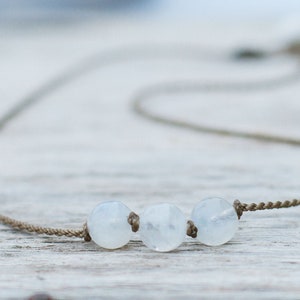 May include: A simple necklace with three white moonstone beads on a brown cord.