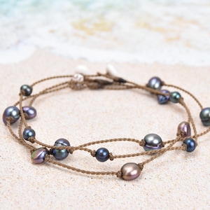 May include: A brown cord necklace with dark iridescent pearls. The necklace is layered and has a simple design.