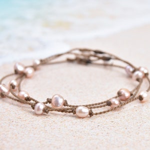 May include: A delicate necklace with pink pearls strung on brown cord. The necklace is layered and features multiple strands of cord and pearls.