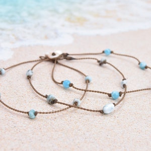 May include: A brown cord necklace with light blue gemstone beads. The necklace is layered and has a shell charm.