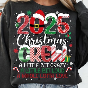 May include: Dark gray sweatshirt with a festive Christmas design. The design includes the text "2025 Christmas CREW" in red, green, and white, with Santa hat accents and candy canes. Additional text reads "A LITTLE BIT CRAZY, A LITTLE BIT LOUD, A WHOLE LOTTA LOVE."