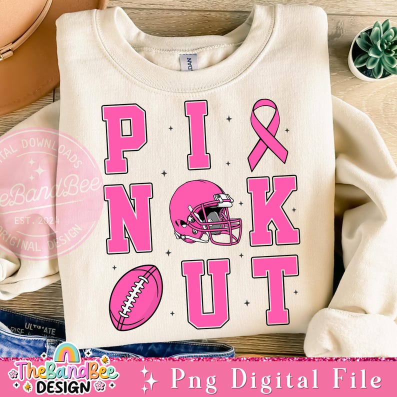 K&ouml;nnte beinhalten: Rosa Sweatshirt mit den Worten "PINK OUT" in gro&szlig;en rosa Buchstaben, einem rosa Band, einem Fu&szlig;ball und einem Footballhelm. Die Worte "The Band Bee Design" befinden sich am unteren Rand des Bildes.