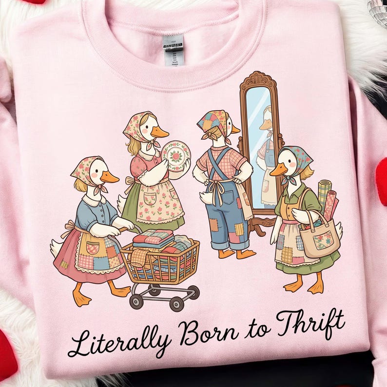 May include: Pink sweatshirt featuring a whimsical illustration of anthropomorphic geese dressed in vintage attire, engaged in thrifting activities. The phrase "Literally Born to Thrift" is printed in a cursive font below the illustration. The geese are depicted with aprons, bandanas, and carrying shopping baskets.