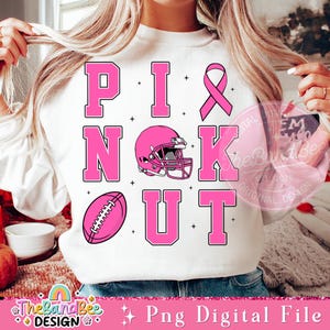 K&ouml;nnte beinhalten: Rosa-wei&szlig;es Grafikdesign mit dem Text "Pink Knockout", einem Footballhelm und einem Football. Das Design ist auf einem wei&szlig;en Sweatshirt.