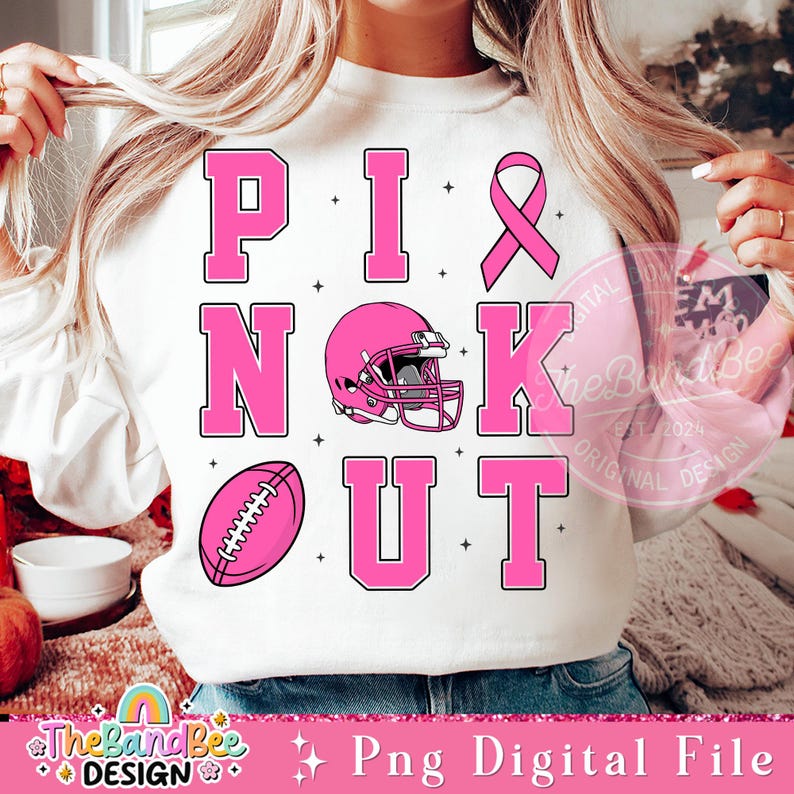 K&ouml;nnte beinhalten: Rosa-wei&szlig;es Grafikdesign mit dem Text "Pink Knockout", einem Footballhelm und einem Football. Das Design ist auf einem wei&szlig;en Sweatshirt.