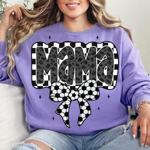 May include: Purple sweatshirt with a black and white chequered design and the word "Mama" in black with a leopard print pattern. A black and white football bow is below the word.