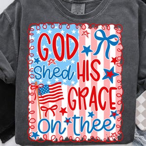 May include: Dark gray sweatshirt with a patriotic design. The graphic features the text "GOD SHED HIS GRACE ON THEE" in red and blue, with an American flag and star accents. The design is framed with a red and white border.