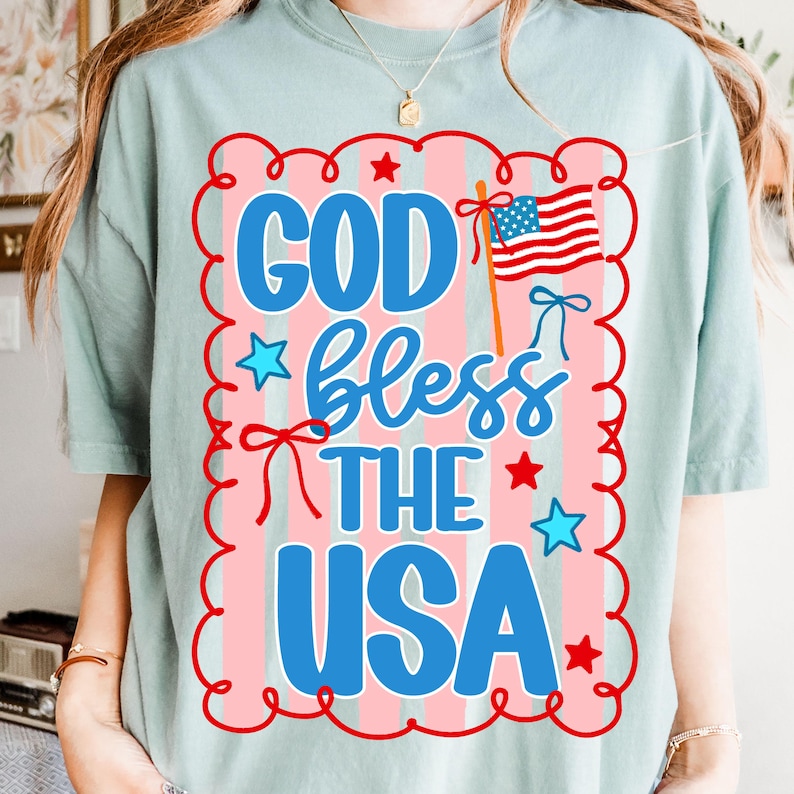Puede incluir: Camiseta verde claro con un dise&ntilde;o patri&oacute;tico. El dise&ntilde;o presenta el texto "GOD bless THE USA" en azul, rojo y blanco, junto con una bandera estadounidense y estrellas. El dise&ntilde;o est&aacute; enmarcado por un borde rojo y rosa.