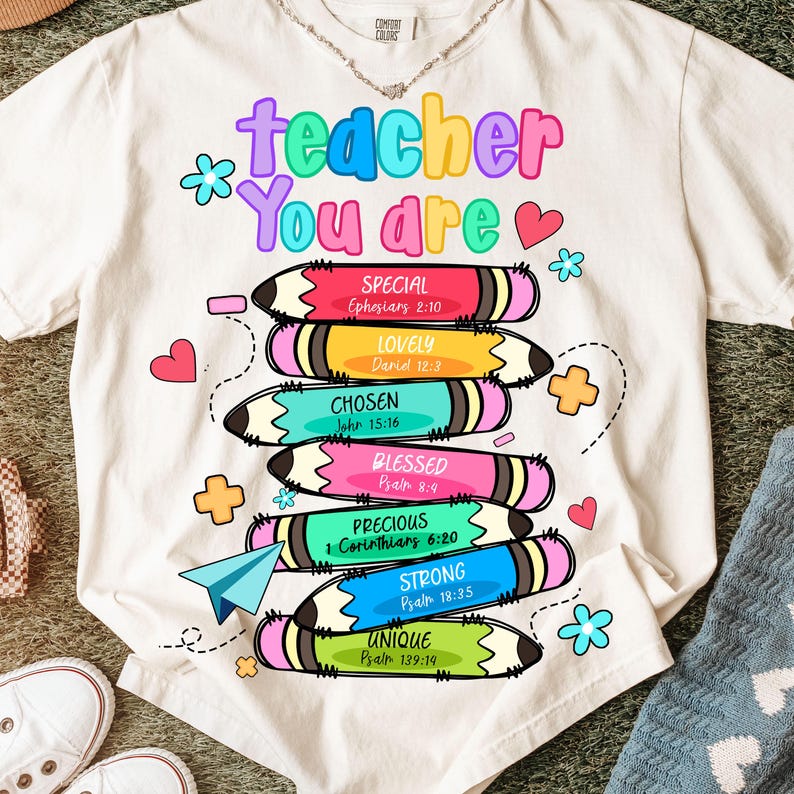 May include: White t-shirt with the text "teacher You are" in colorful letters. Below the text are stacked pencils with words like "Special", "Lovely", and "Chosen". The shirt has a casual, relaxed fit, suitable for everyday wear.