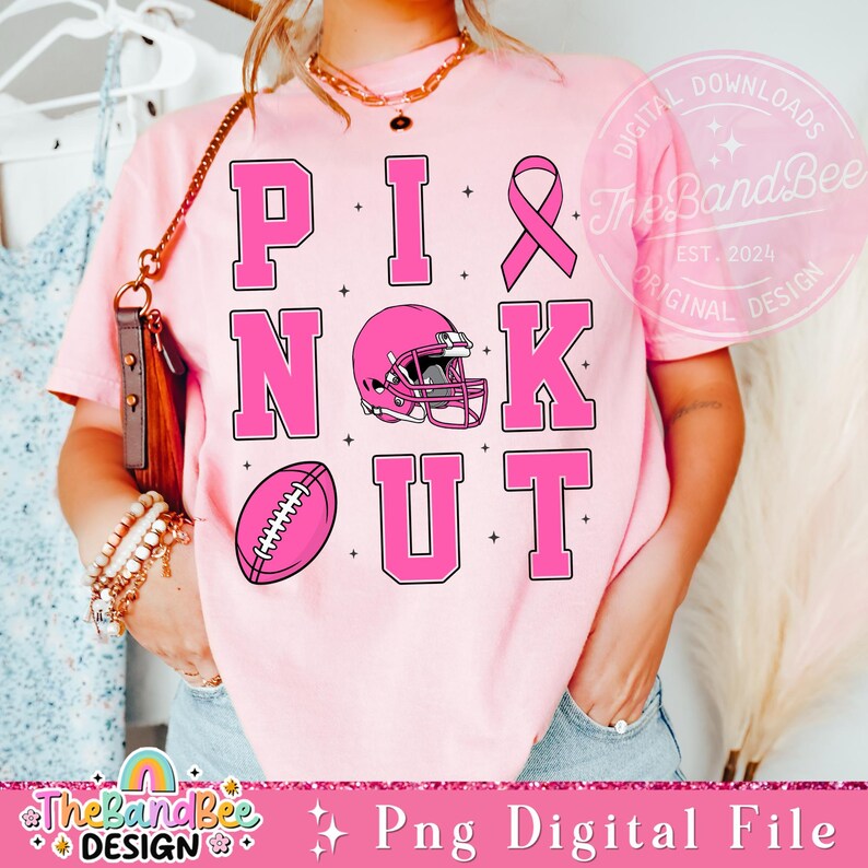 K&ouml;nnte beinhalten: Pinkes T-Shirt mit dem Text "PINK OUT" in gro&szlig;en pinkfarbenen Buchstaben. Ein pinkfarbener Fu&szlig;ball und ein pinkfarbener Footballhelm sind im Design enthalten. Ein pinkfarbenes Band ist ebenfalls im Design enthalten.